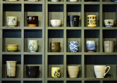 Collection of colorful ceramic mugs showcased on a wooden shelf in grid design.