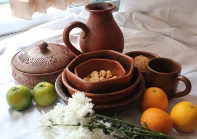 A still life arrangement of rustic clay pottery alongside fresh citrus fruits and white flowers.
